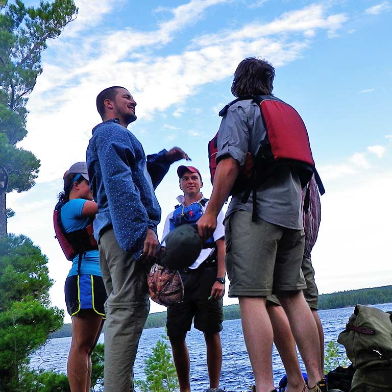 A group of students stands on the shore of a lake.